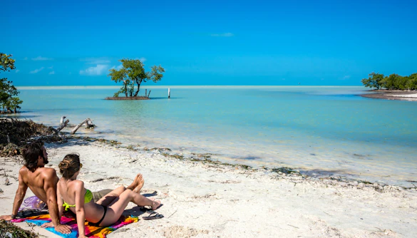 Couple relaxing on a sandy beach at Holbox Island, Mexico, with turquoise water and clear sky.
