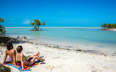 Couple relaxing on a sandy beach at Holbox Island, Mexico, with turquoise water and clear sky.