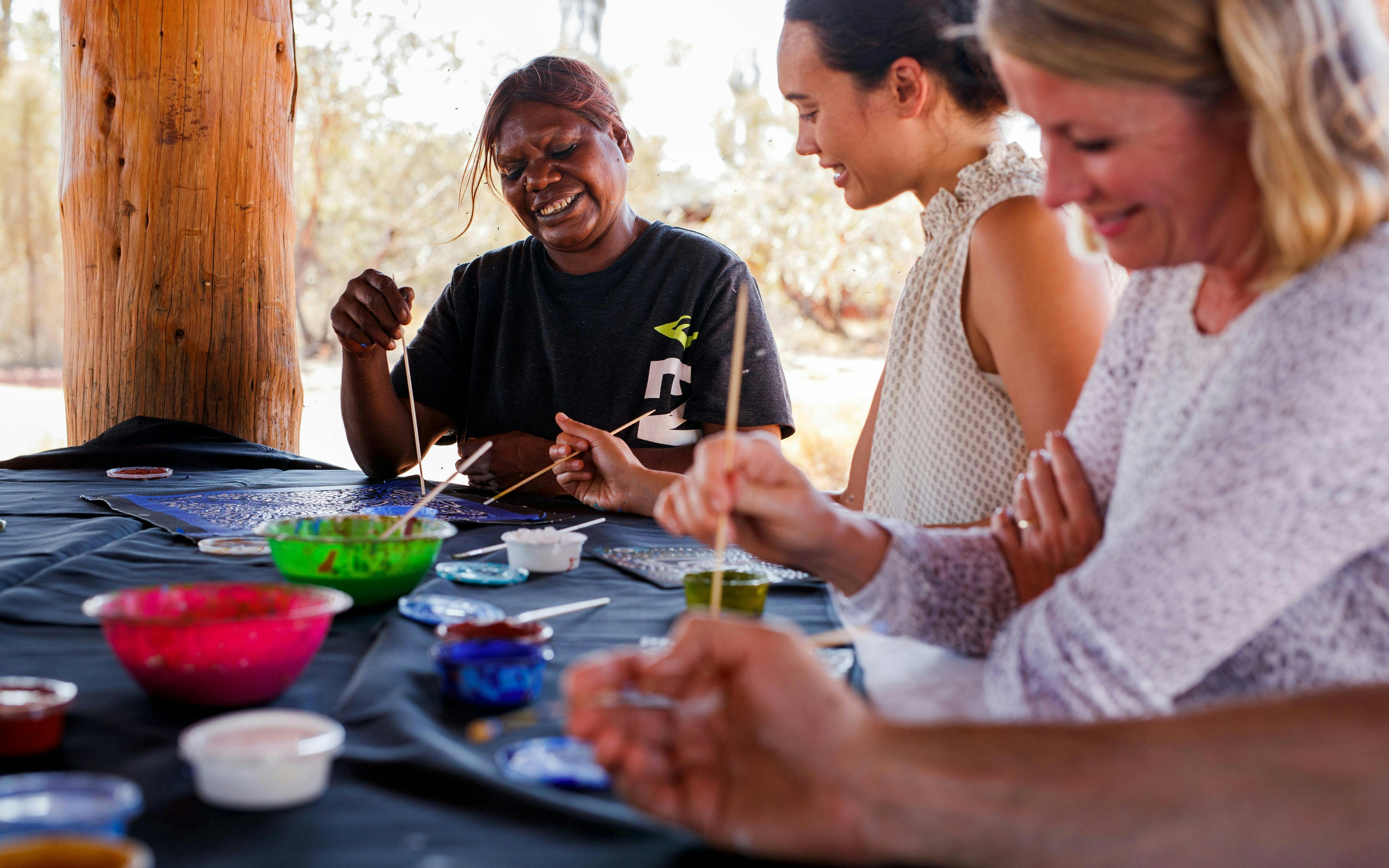 Participants painting with Aboriginal artist during Uluru sunrise tour.