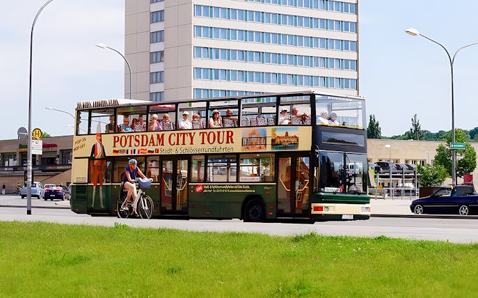 Potsdam city tour bus with tourists on upper deck near modern building.