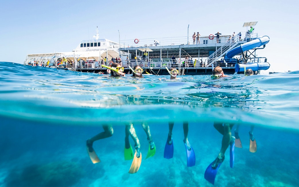 Tourists snorkeling at Moore Reef, Great Barrier Reef near a boat in clear blue waters.
