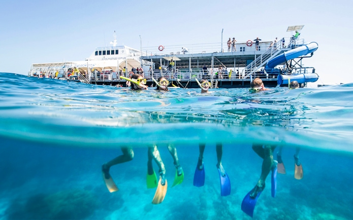 Tourists snorkeling at Moore Reef, Great Barrier Reef near a boat in clear blue waters.