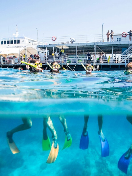 Tourists snorkeling at Moore Reef, Great Barrier Reef near a boat in clear blue waters.