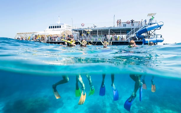 Tourists snorkeling at Moore Reef, Great Barrier Reef near a boat in clear blue waters.