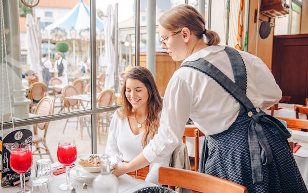 Waitress serving a smiling guest at Puy Du Fou restaurant, France.