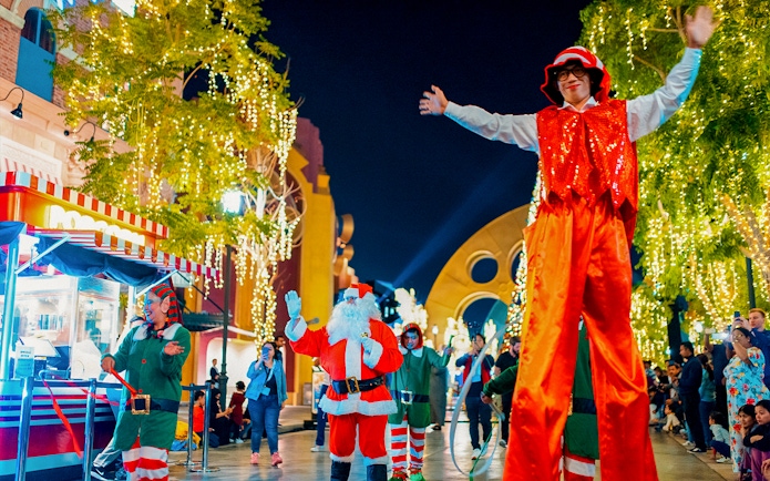 Festive performers and Santa at MOTIONGATE™ Dubai during a nighttime event.