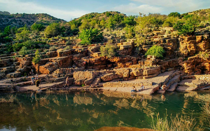 Rocky landscape with visitors by a river in Paradise Valley, surrounded by greenery and hills.