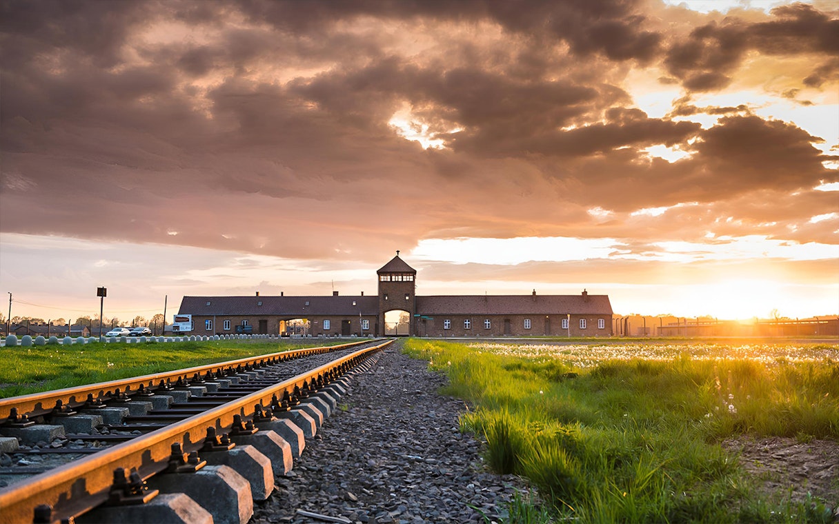 Railway tracks leading to Auschwitz-Birkenau entrance at sunset, Poland.