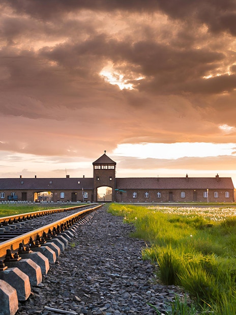 Railway tracks leading to Auschwitz-Birkenau entrance at sunset, Poland.