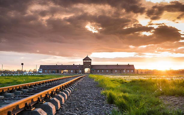 Railway tracks leading to Auschwitz-Birkenau entrance at sunset, Poland.