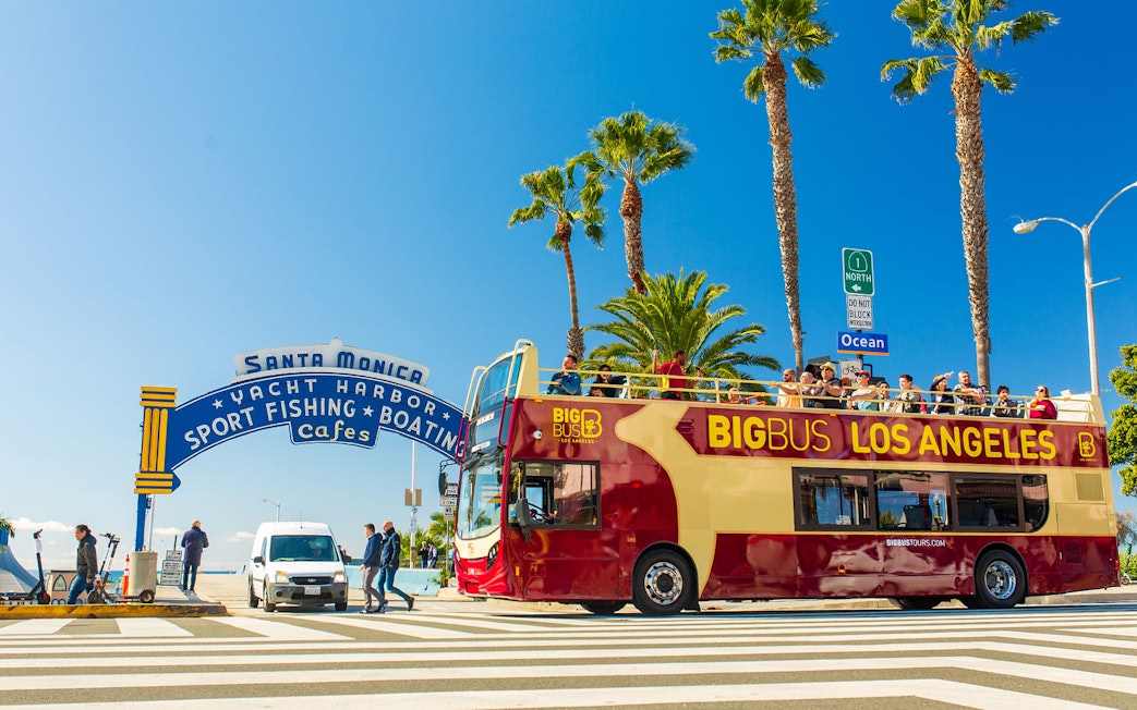Open-top tour bus near Santa Monica Pier sign on Los Angeles Hop-On Hop-Off Tour.
