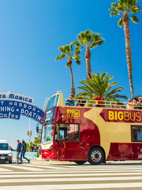 Open-top tour bus near Santa Monica Pier sign on Los Angeles Hop-On Hop-Off Tour.