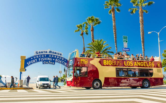Open-top tour bus near Santa Monica Pier sign on Los Angeles Hop-On Hop-Off Tour.
