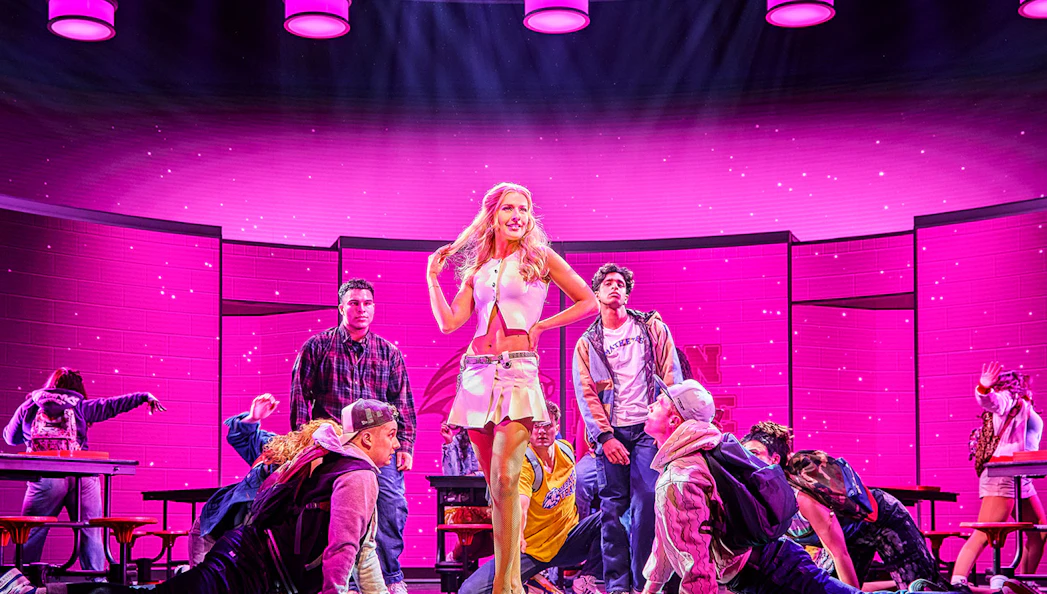 Performers on stage during Mean Girls The Musical with a vibrant pink backdrop.