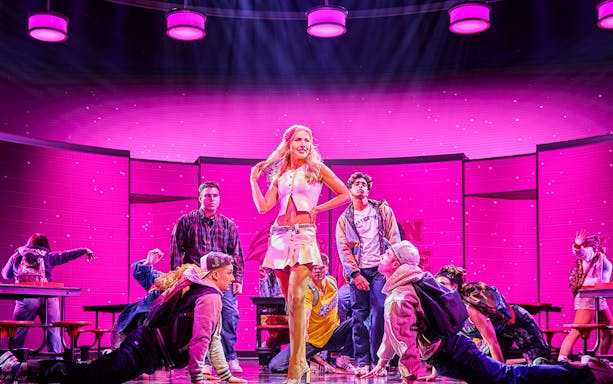 Performers on stage during Mean Girls The Musical with a vibrant pink backdrop.