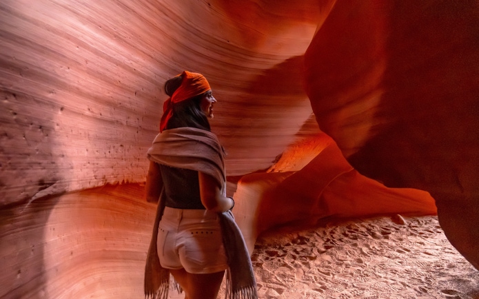 Woman walking through Antelope Canyon's narrow sandstone walls.