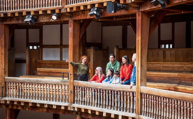 Tour guide pointing out features of Shakespeare's Globe Theatre to a group of visitors.