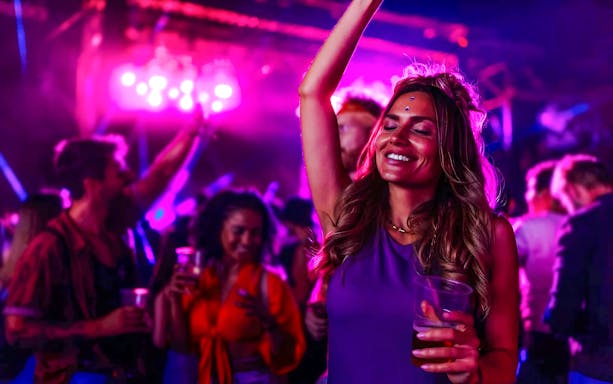 Tourists dancing and enjoying a vibrant party with colorful lights.