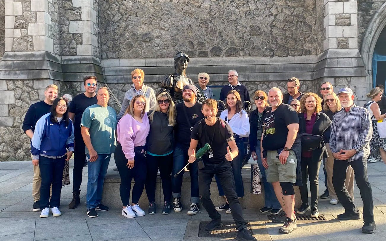 Tour guide with tourists near a statue at Trinity College, Dublin.