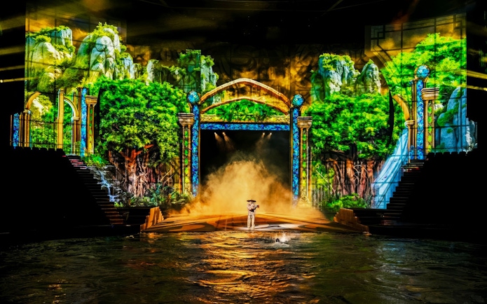 Performer on water platform with green trees backdrop at House of Dancing Water Show.