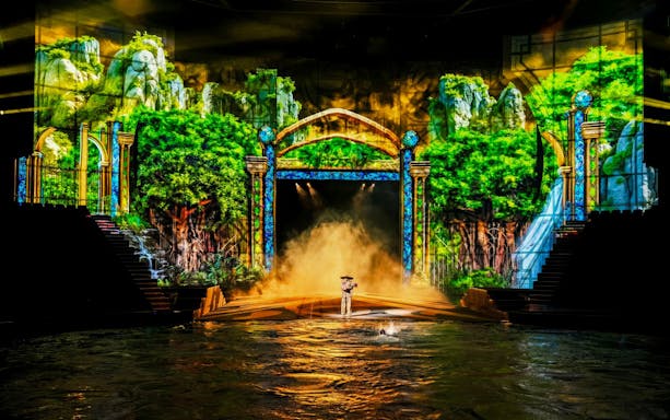 Performer on water platform with green trees backdrop at House of Dancing Water Show.