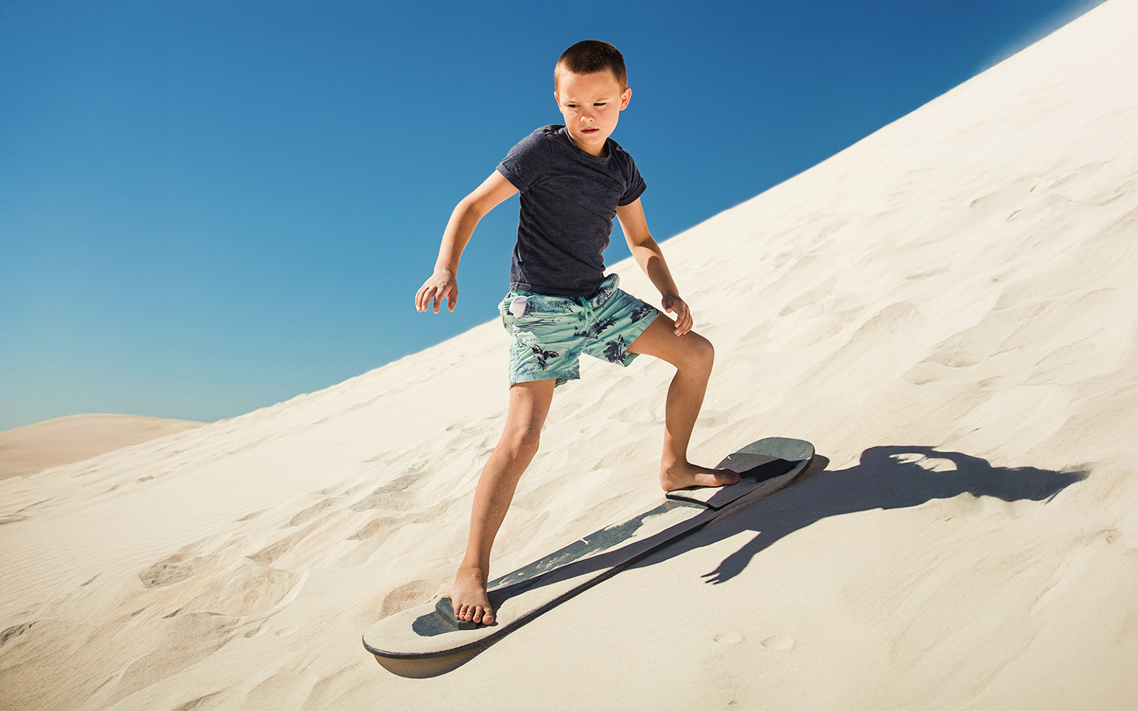 Child sandboarding down a sunny dune.