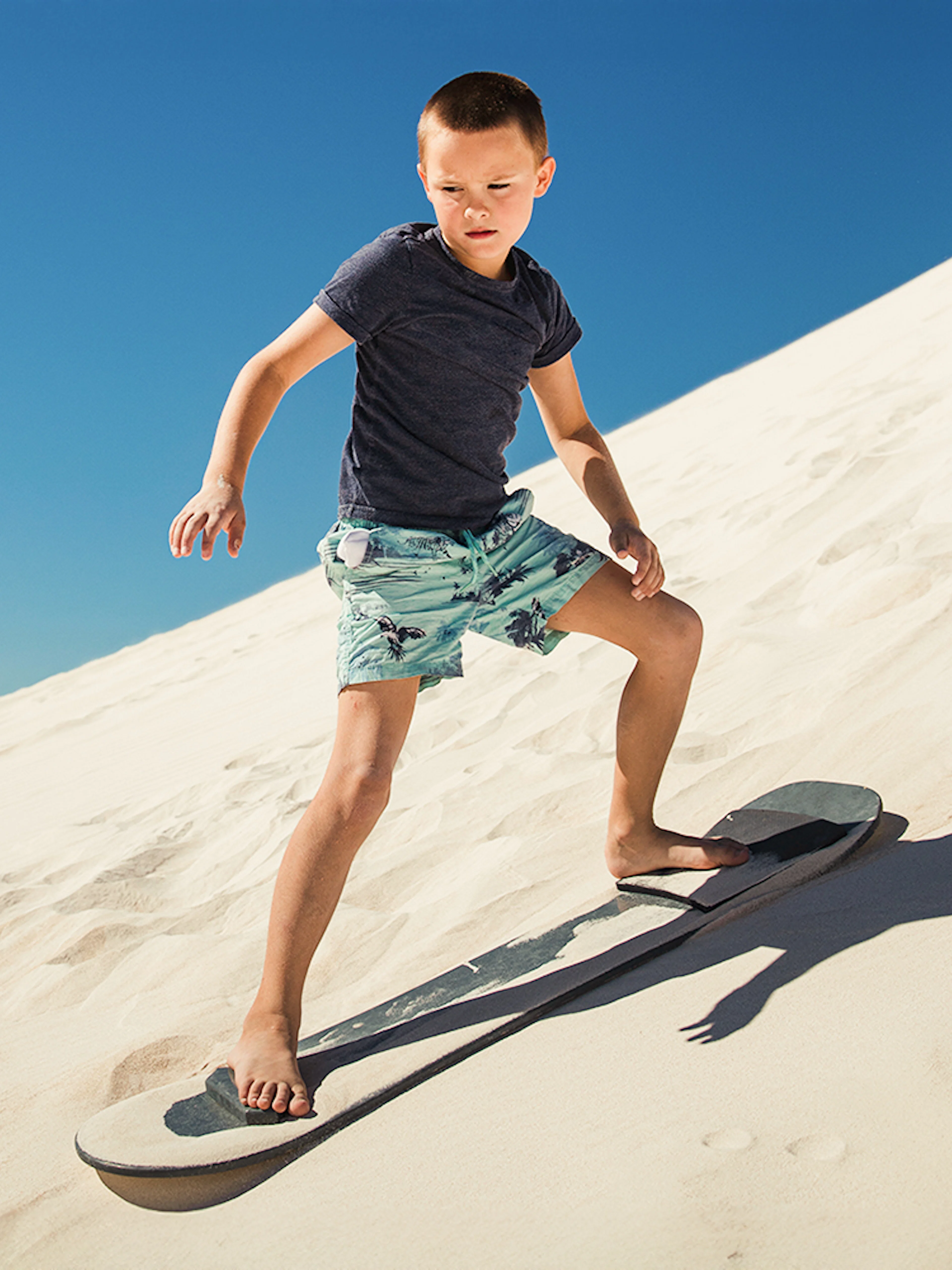 Child sandboarding down a sunny dune.