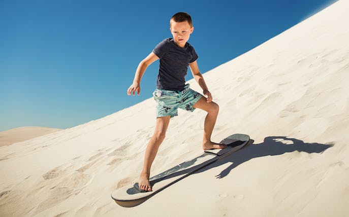 Child sandboarding down a sunny dune.