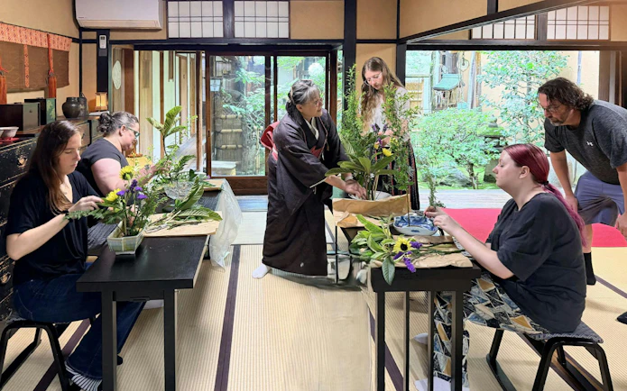 Tourists practicing ikebana in a traditional Kyoto room with a Japanese instructor.