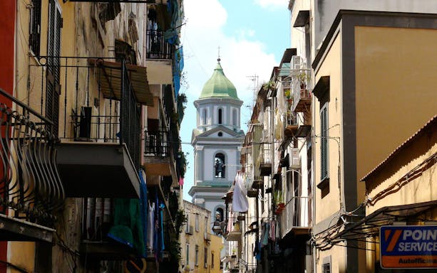 Narrow street in Naples' Rione Sanità with view of church tower.
