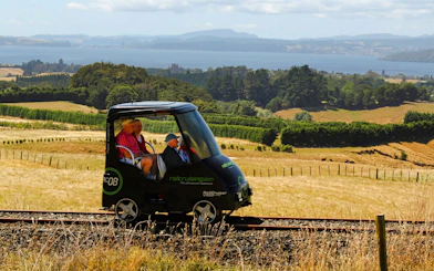 Self-drive rail car on tracks with scenic view of Ngongotaha countryside and lake in background.
