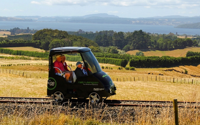 Self-drive rail car on tracks with scenic view of Ngongotaha countryside and lake in background.