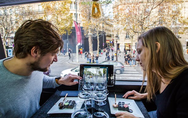 Couple dining inside Bus Toqué Paris with city view through window.