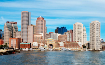 Boston skyline viewed from the harbor with prominent skyscrapers and waterfront.