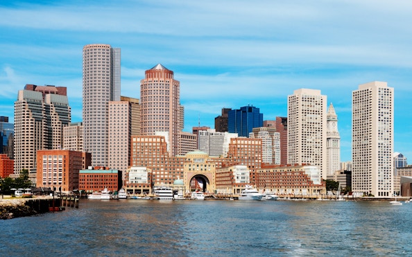 Boston skyline viewed from the harbor with prominent skyscrapers and waterfront.
