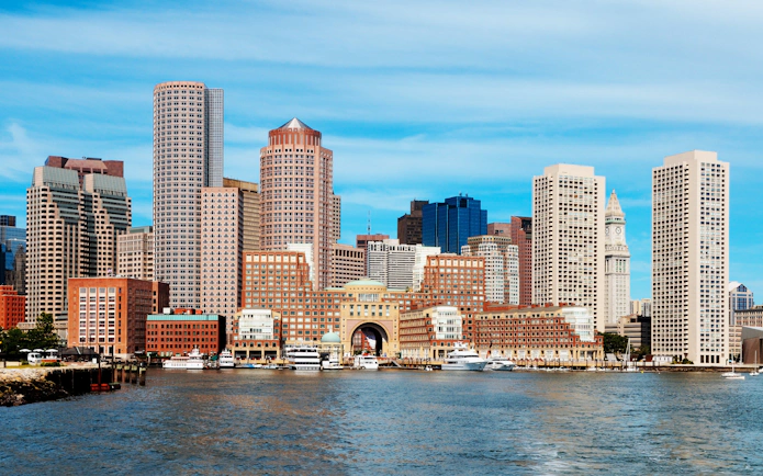 Boston skyline viewed from the harbor with prominent skyscrapers and waterfront.