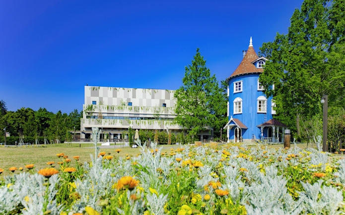 Moominvalley Park blue house with garden and modern building in background.