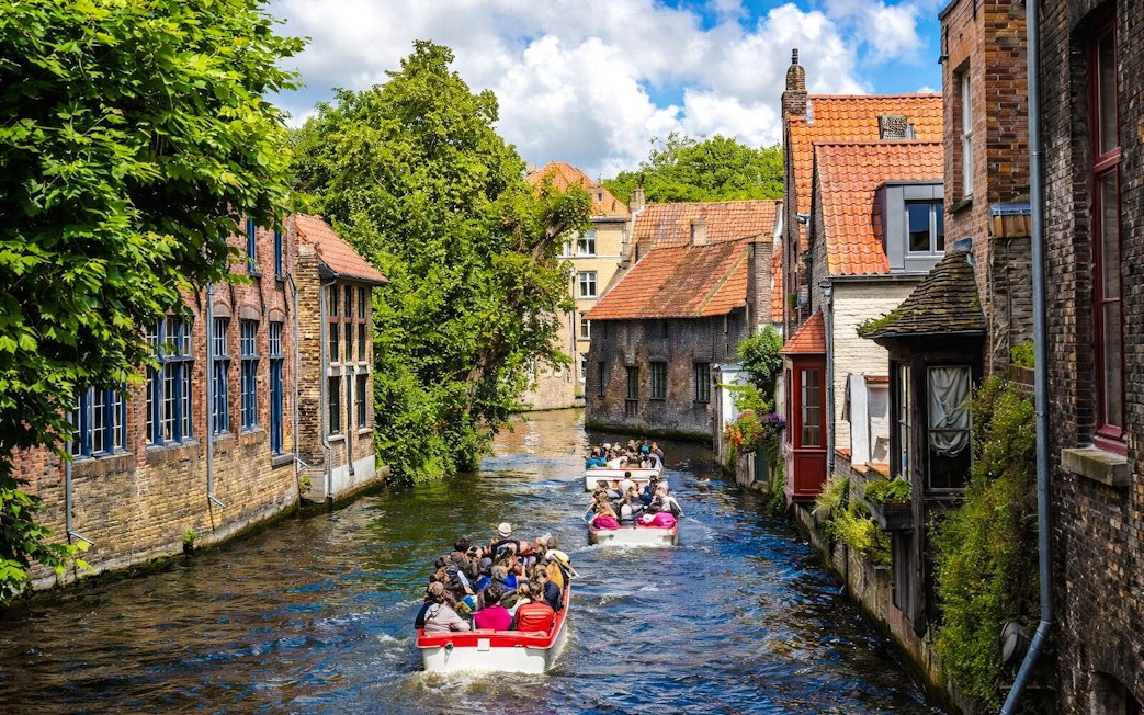 Guests enjoying a boat ride through the canals of Bruges, Belgium, surrounded by historic buildings.