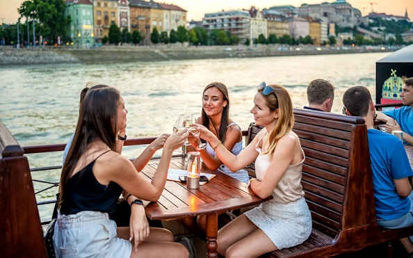 Guests enjoying drinks on a Budapest river cruise with cityscape views.