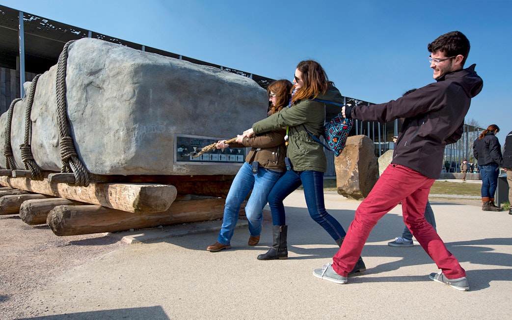 Visitors pulling a rope to move a large stone at Stonehenge exhibit, England.