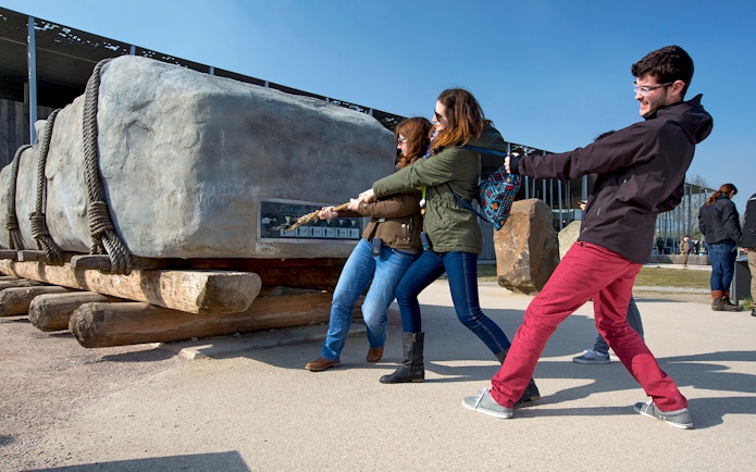 Visitors pulling a rope to move a large stone at Stonehenge exhibit, England.