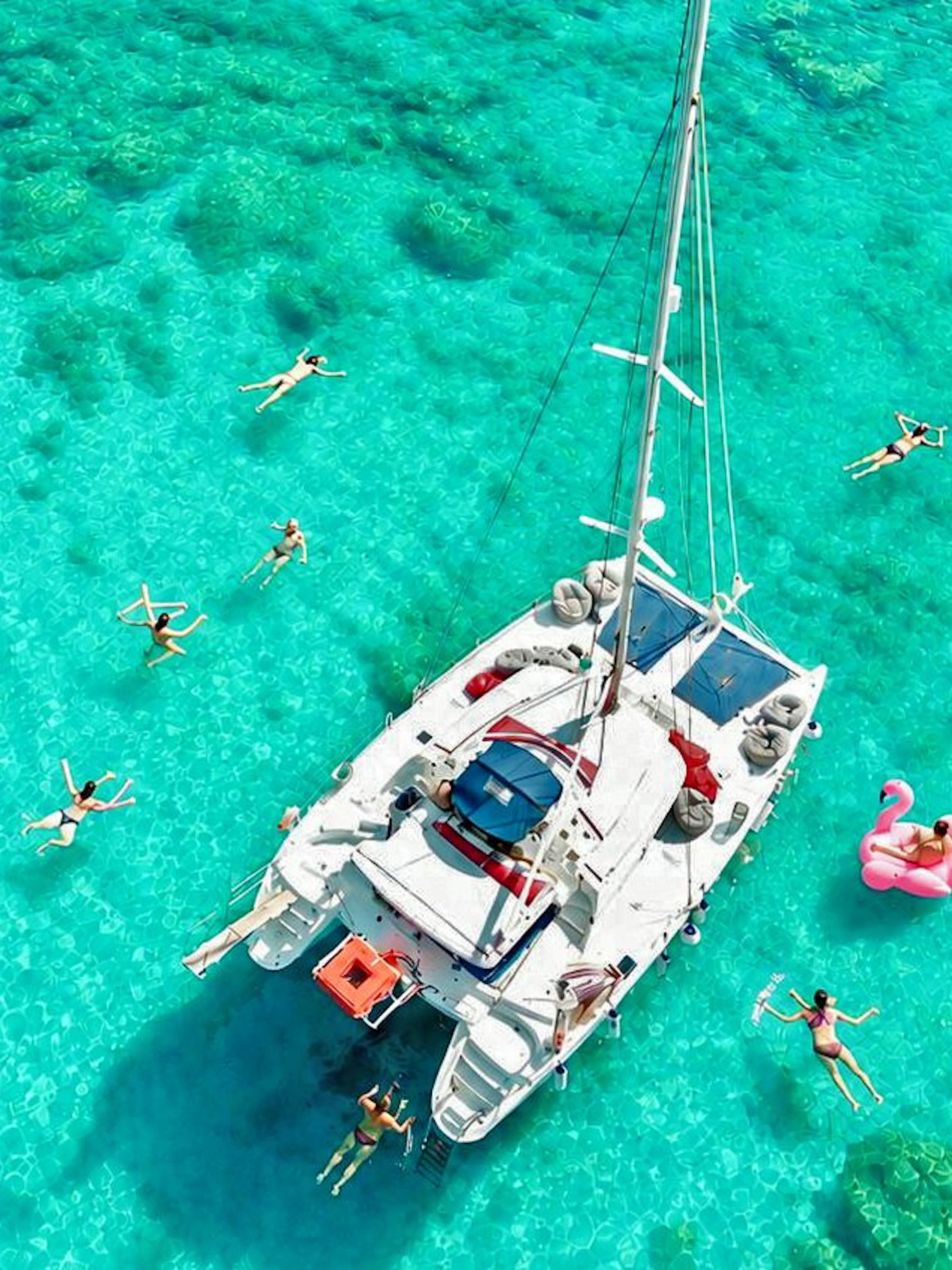 Catamaran surrounded by people swimming and paddleboarding in clear waters, Rhodes.