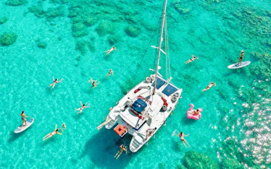 Catamaran surrounded by people swimming and paddleboarding in clear waters, Rhodes.