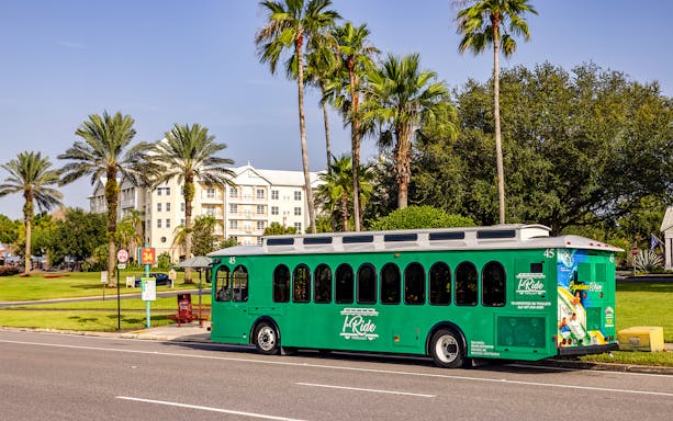 Orlando I-Ride trolley bus parked near palm trees and a residential building.