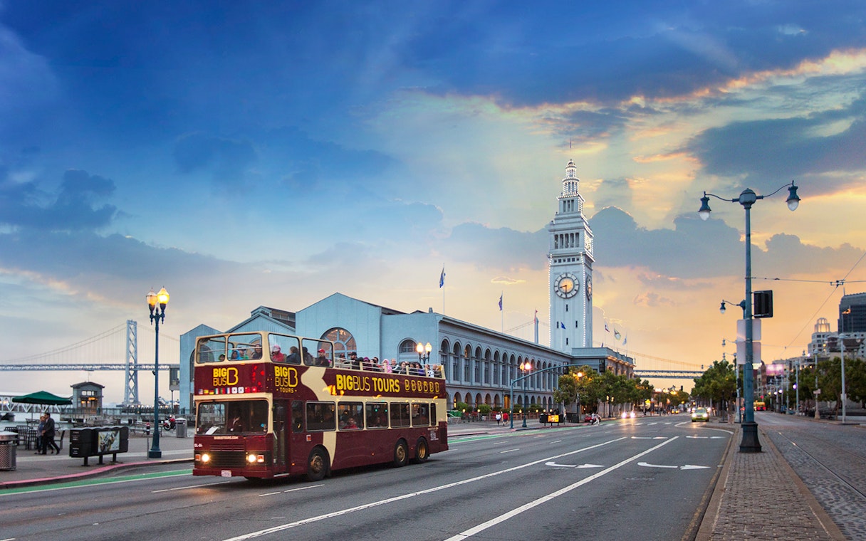 Big Bus passing San Francisco Ferry Building during sunset tour.