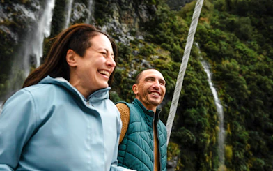 Couple laughing on a boat with waterfall and cliffs in Doubtful Sound, New Zealand.