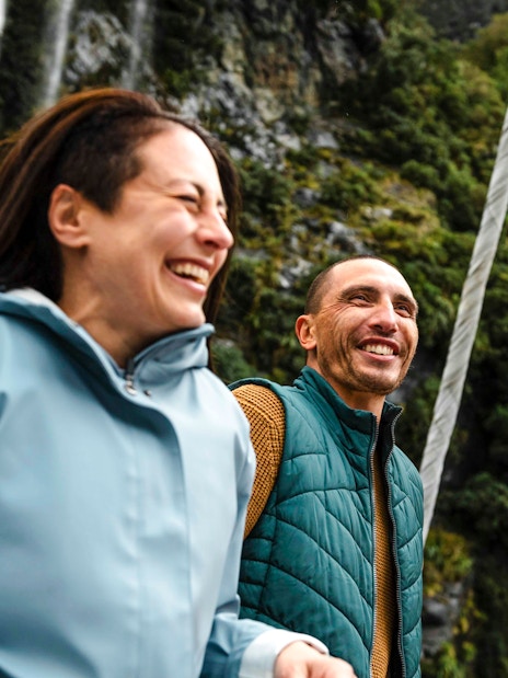 Couple laughing on a boat with waterfall and cliffs in Doubtful Sound, New Zealand.