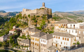 Gjirokaster Castle with clock tower overlooking traditional stone houses.
