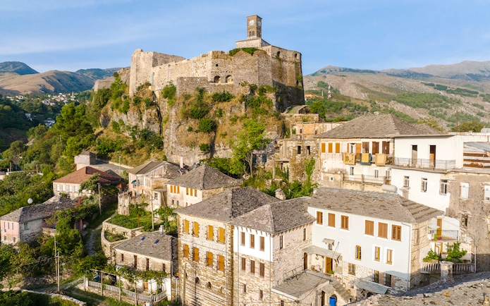 Gjirokaster Castle with clock tower overlooking traditional stone houses.