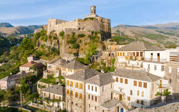 Gjirokaster Castle with clock tower overlooking traditional stone houses.
